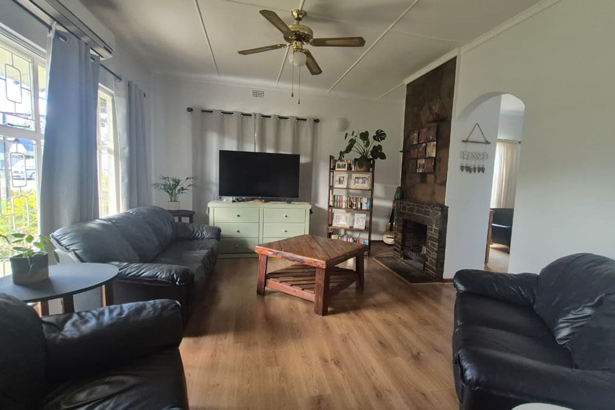 A comfortable living room featuring laminate flooring, a ceiling fan, an air conditioning unit, and a traditional fireplace with a brick surround.