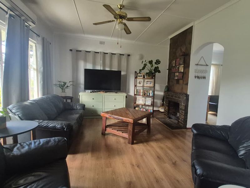 A comfortable living room featuring laminate flooring, a ceiling fan, an air conditioning unit, and a traditional fireplace with a brick surround.