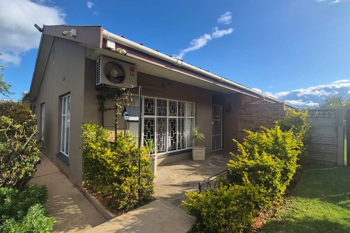 A well-maintained rear exterior view featuring a stone-paved patio, security-fitted windows, and an integrated air conditioning unit set against a landscaped garden.