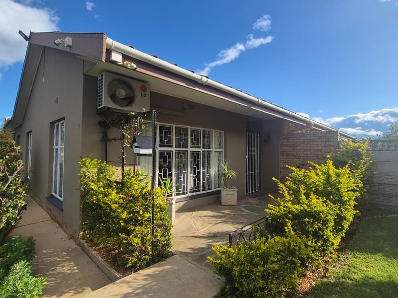 A well-maintained rear exterior view featuring a stone-paved patio, security-fitted windows, and an integrated air conditioning unit set against a landscaped garden.