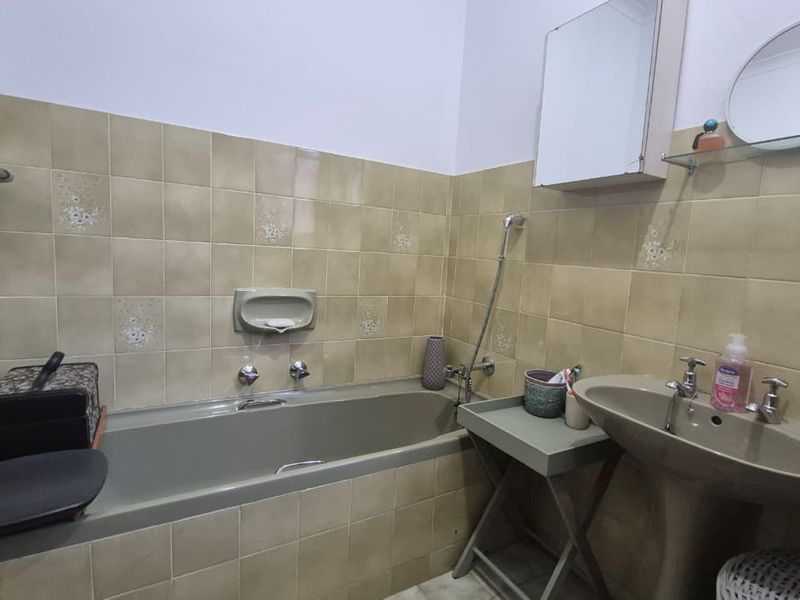 A functional bathroom featuring a bathtub, pedestal basin, and wall-mounted medicine cabinet with dated wall tiling throughout.