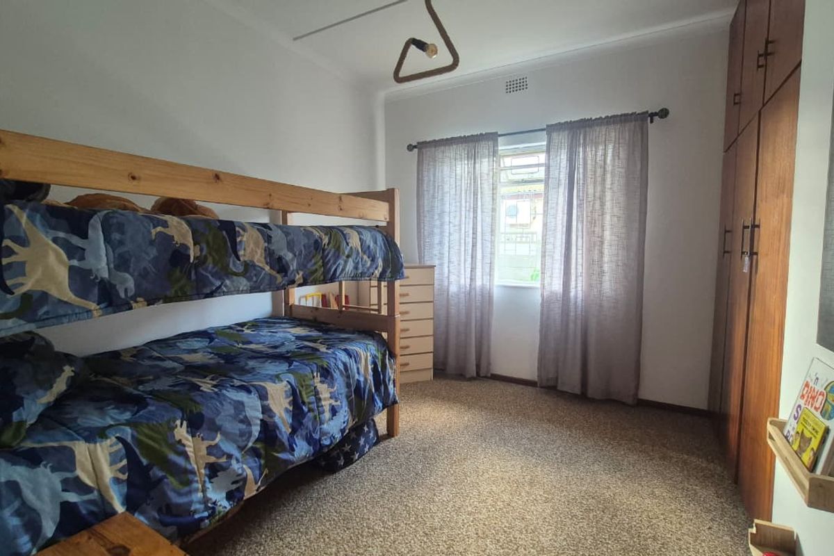 A functional bedroom featuring built-in wooden cupboards, carpeted flooring, and a window with curtain rods, providing a practical space for residents.