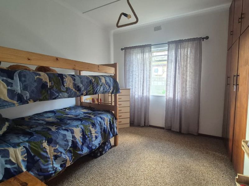 A functional bedroom featuring built-in wooden cupboards, carpeted flooring, and a window with curtain rods, providing a practical space for residents.