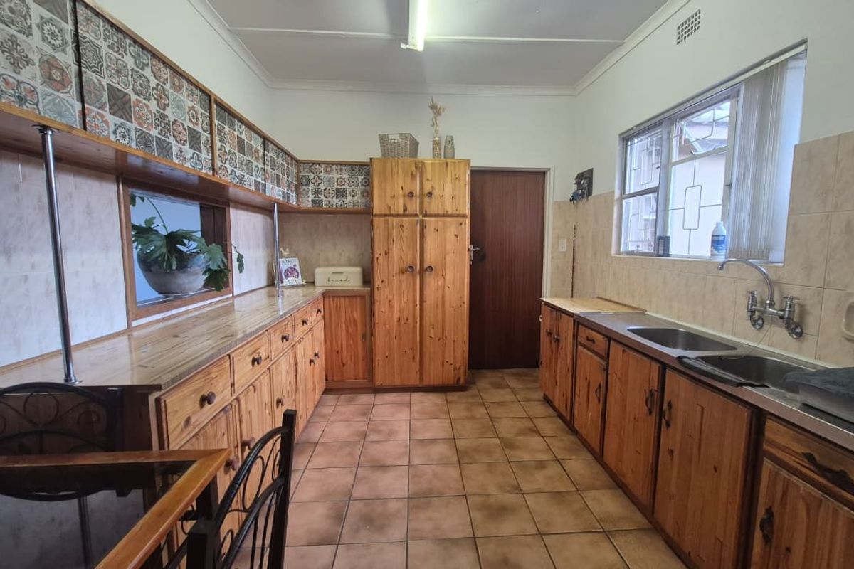 A functional kitchen featuring extensive wooden cabinetry, tiled backsplash, and a double stainless steel sink with tiled flooring throughout.