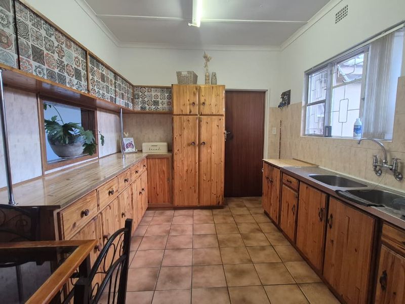 A functional kitchen featuring extensive wooden cabinetry, tiled backsplash, and a double stainless steel sink with tiled flooring throughout.