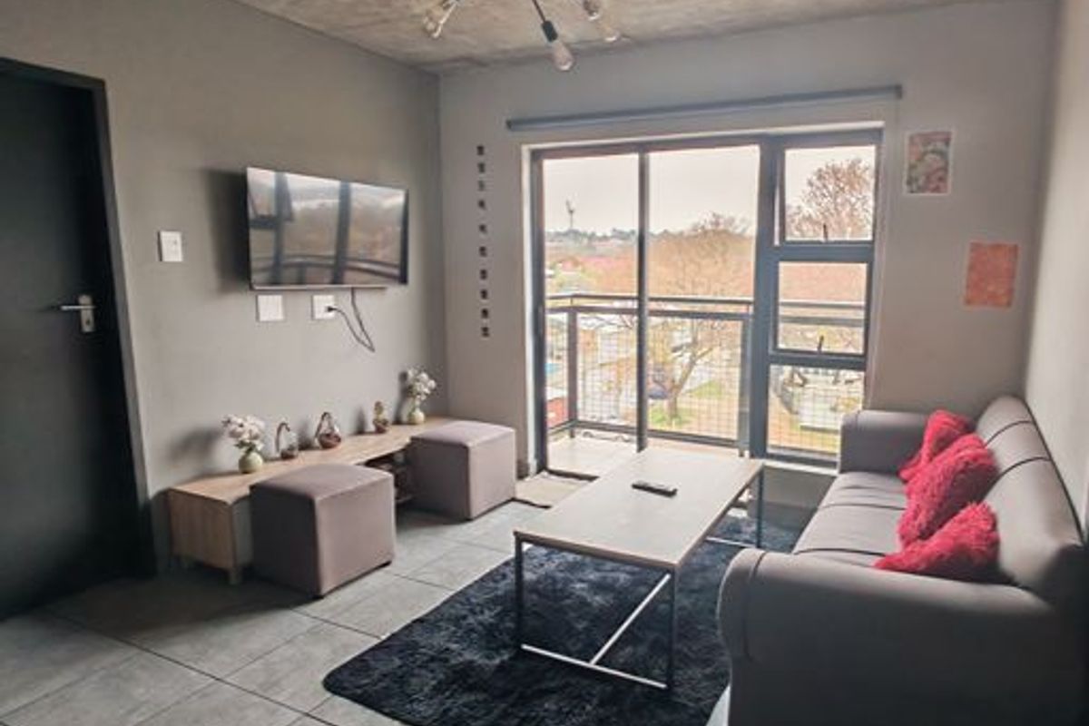 Modern living room featuring an exposed concrete ceiling, large sliding glass doors leading to a balcony, and neutral tiled flooring.