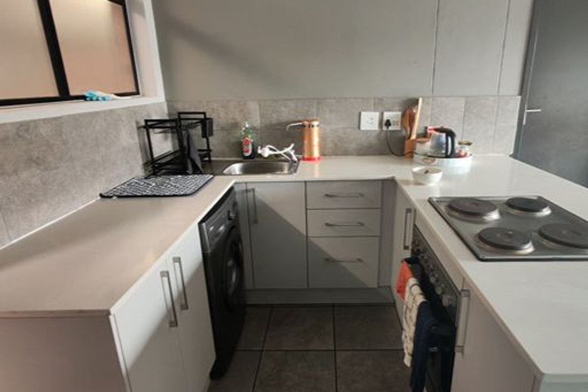 A functional kitchen featuring modern white cabinetry, stone countertops, a built-in electric hob and oven, and tiled flooring.
