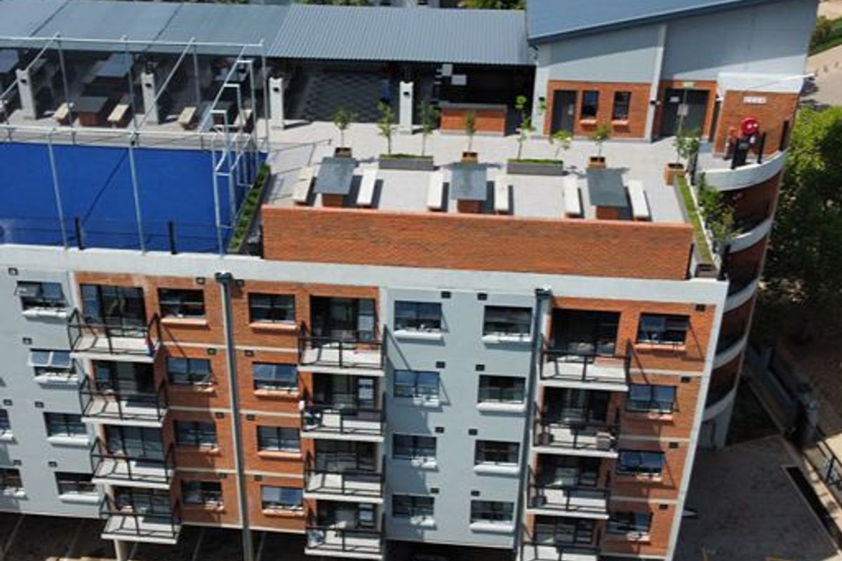 Aerial view of a modern apartment complex featuring a rooftop terrace with a swimming pool, private balconies, and ground-level parking facilities.