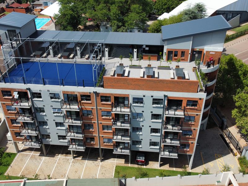 Aerial view of a modern apartment building featuring a rooftop sports court, communal seating areas, private balconies, and ground-level covered parking.
