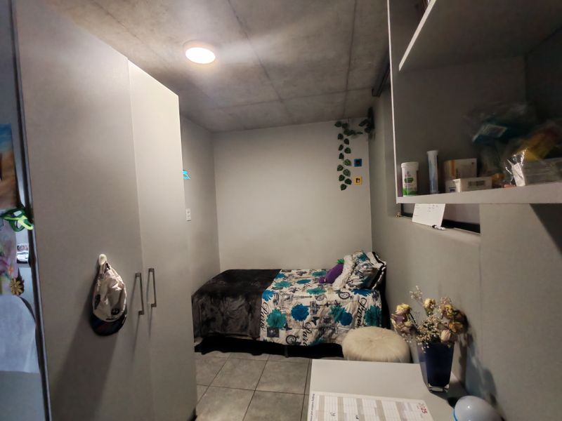 Compact bedroom featuring built-in wardrobe storage, integrated shelving, tiled flooring, and a modern concrete-look ceiling finish.
