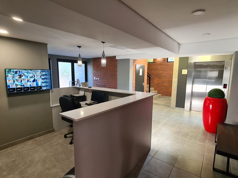 Modern apartment building entrance lobby featuring a reception desk, elevator access, and contemporary finishes with exposed brick accents.