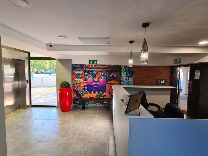 A modern apartment building entrance lobby featuring a reception desk, elevator access, tiled flooring, and decorative mural wall.