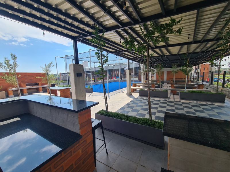 Spacious covered outdoor patio featuring built-in brick braai stations, granite countertops, and integrated planters, overlooking a recreational sports area.