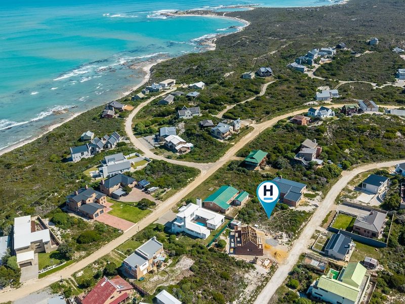 Aerial view of a coastal residential estate featuring established homes and vacant plots near the ocean.