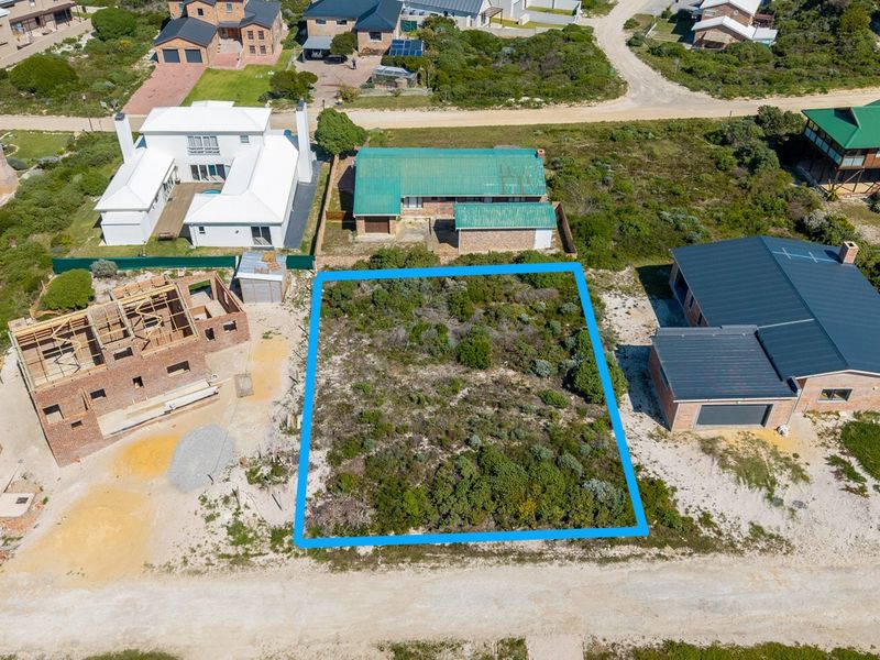 An aerial view of a vacant residential plot situated in a coastal neighborhood, surrounded by existing homes and ongoing construction.