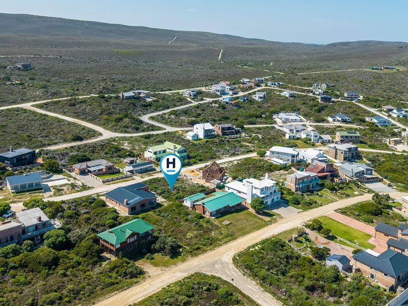 An aerial view of a vacant residential plot situated within a coastal estate, surrounded by established homes and natural fynbos vegetation.