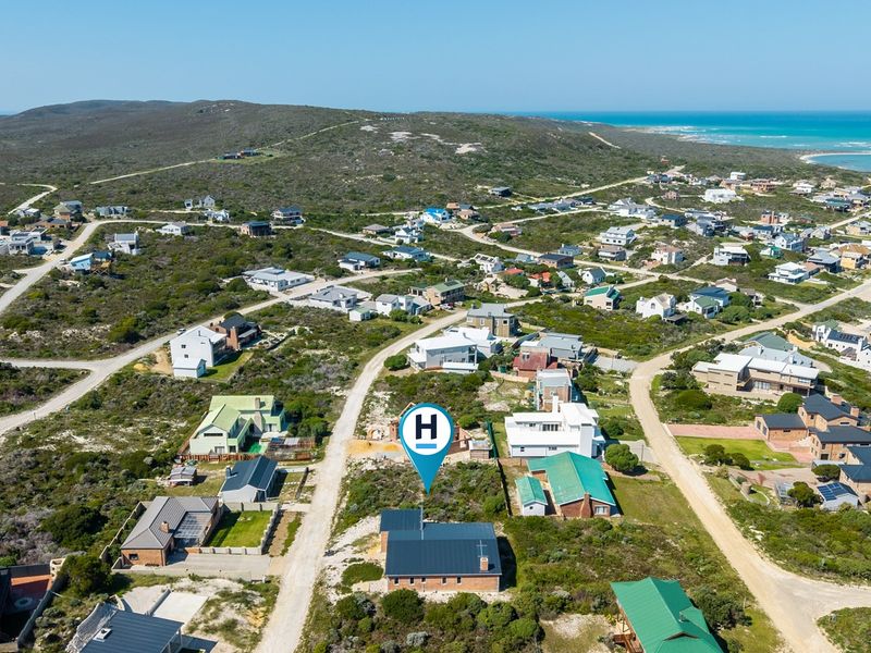 Aerial view of a residential coastal development featuring scattered homes, natural vegetation, and unpaved access roads near the ocean.