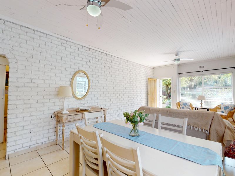 Spacious open-plan living and dining area featuring a white-painted exposed brick wall, timber ceiling, and tiled flooring with direct access to the garden.
