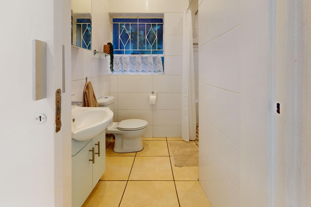 A functional bathroom featuring tiled walls and flooring, a pedestal washbasin, toilet, and a shower area with a curtain.