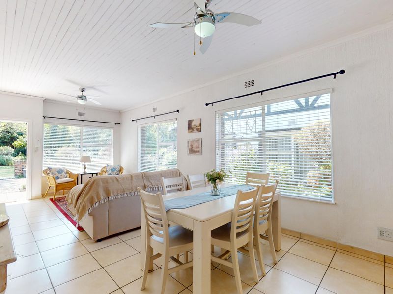 Bright open-plan living and dining area featuring tiled floors, timber-look ceilings, ceiling fans, and large windows providing natural light and garden views.