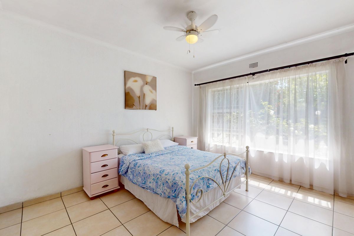 A bright bedroom featuring tiled flooring, built-in cupboards, and a ceiling fan, offering a clean and functional space.