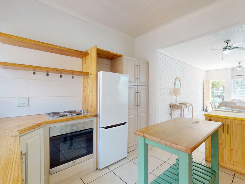 Open-plan kitchen area featuring wooden countertops, built-in oven and hob, and tiled flooring, flowing into a bright living space with exposed brick wall.