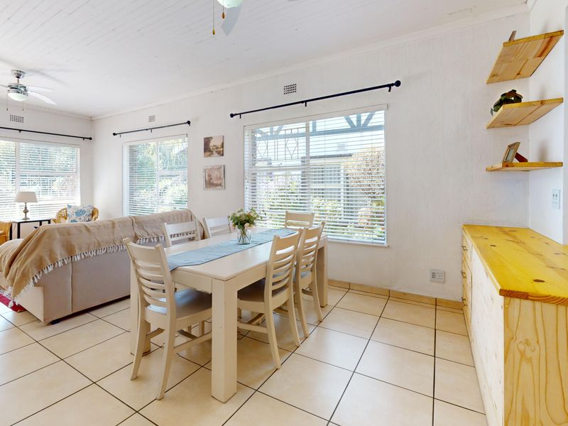 Bright open-plan living and dining area featuring tiled flooring, ceiling fans, and built-in wooden cabinetry with floating shelves.