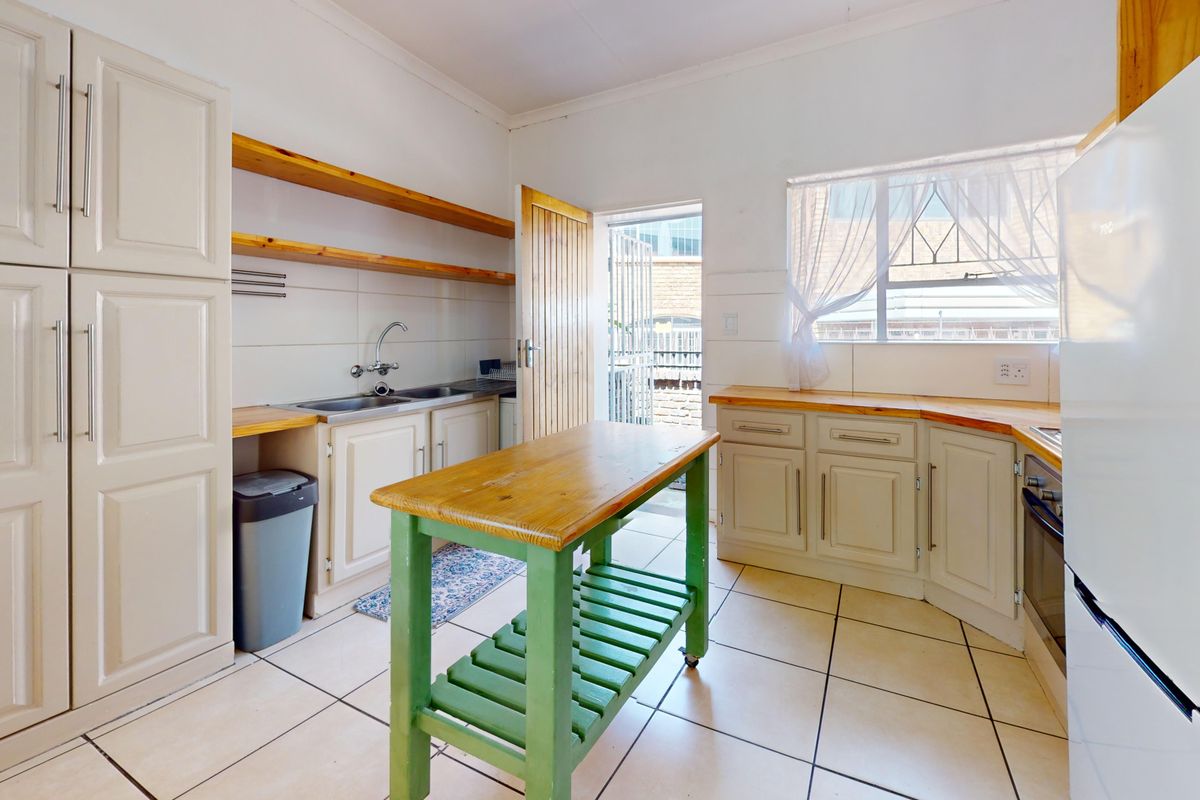 A functional kitchen featuring tiled flooring, wooden countertops, built-in cabinetry, and direct access to an exterior area through a security gate.