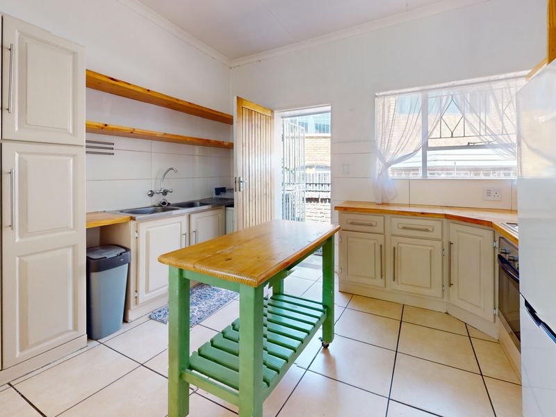 A functional kitchen featuring tiled flooring, wooden countertops, built-in cabinetry, and direct access to an exterior area through a security gate.