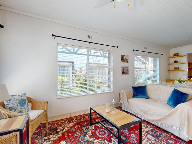Bright open-plan living area featuring tiled floors, a timber panelled ceiling, ceiling fans, and large windows allowing for ample natural light.
