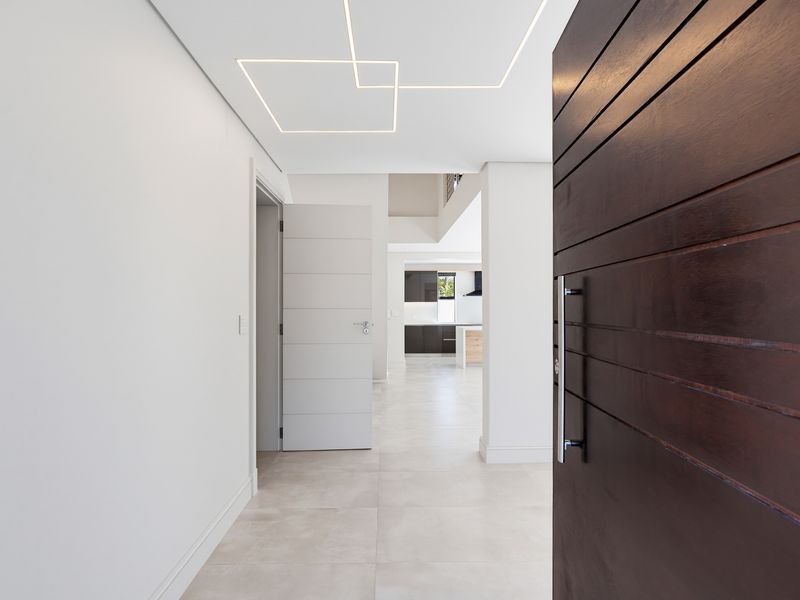 A bright and modern entrance hall featuring large format floor tiles, minimalist linear ceiling lighting, and a substantial dark timber front door.