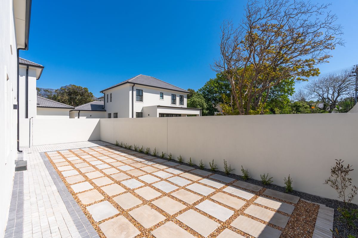 A clean, modern rear courtyard featuring paved square tiles, gravel borders, and a high boundary wall, set against a well-maintained residential property.