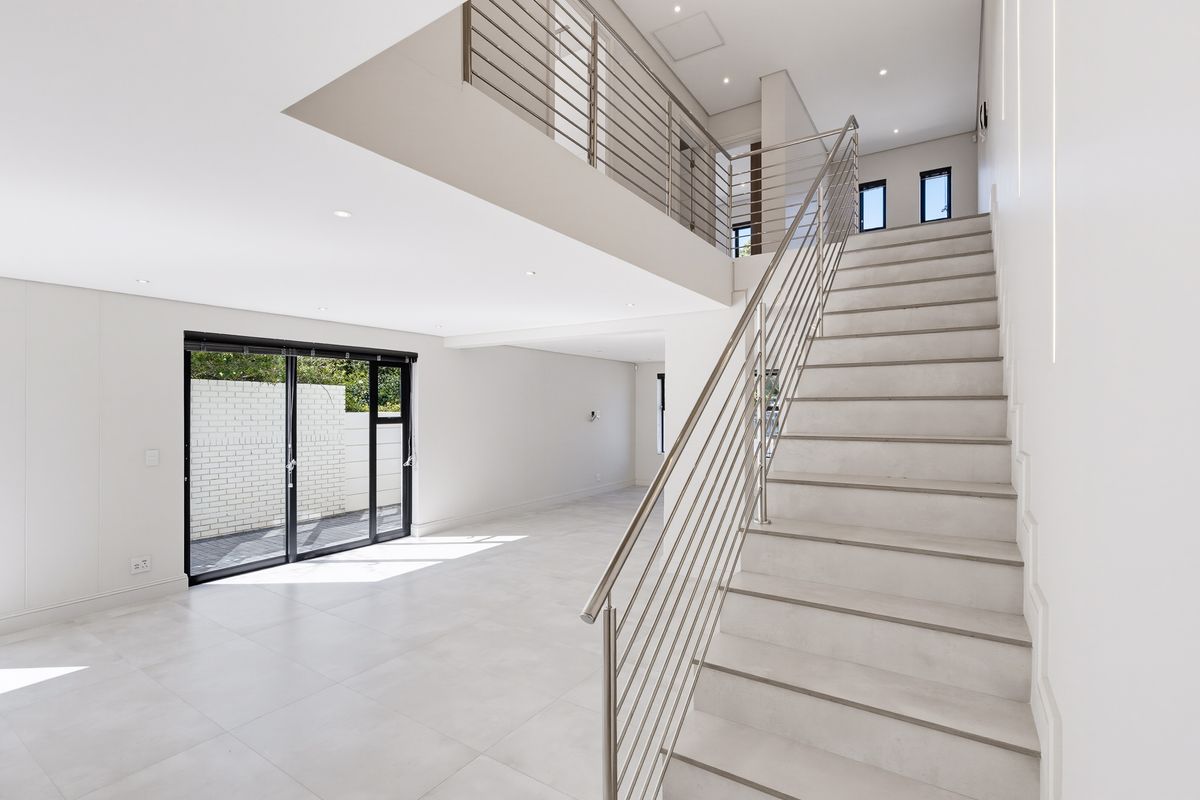 Spacious open-plan living area featuring a modern staircase with stainless steel balustrades, tiled flooring, and large sliding doors leading to the exterior.