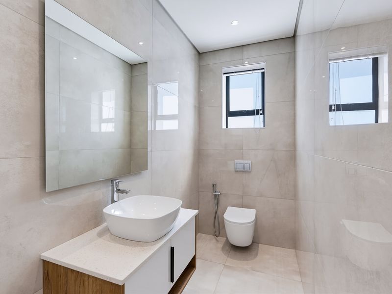 Modern bathroom featuring neutral large-format wall and floor tiles, a sleek vanity with a vessel sink, and a wall-mounted toilet.