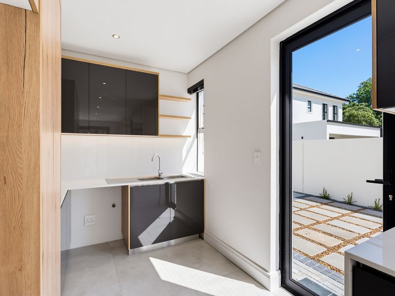 Modern scullery featuring sleek dark cabinetry, floating shelves, stainless steel sink, and direct access to the outdoor patio area.