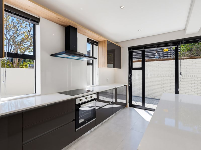 Modern kitchen featuring sleek dark cabinetry, white quartz countertops, integrated appliances, and direct access to the outdoor area through a sliding glass door.