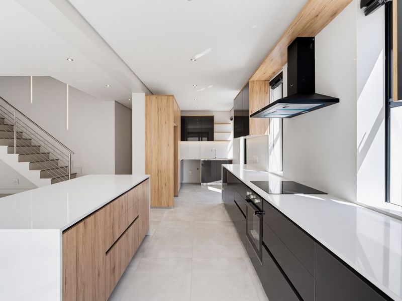 Modern, high-end kitchen featuring sleek cabinetry, quartz countertops, integrated appliances, and a central island, seamlessly connected to an open-plan staircase area.