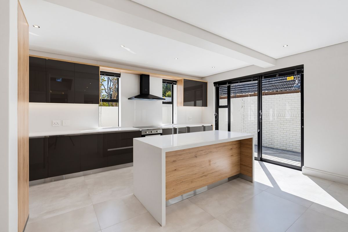 Modern kitchen featuring a central island, quartz countertops, high-gloss cabinetry, built-in appliances, and large glass sliding doors leading to an outdoor area.