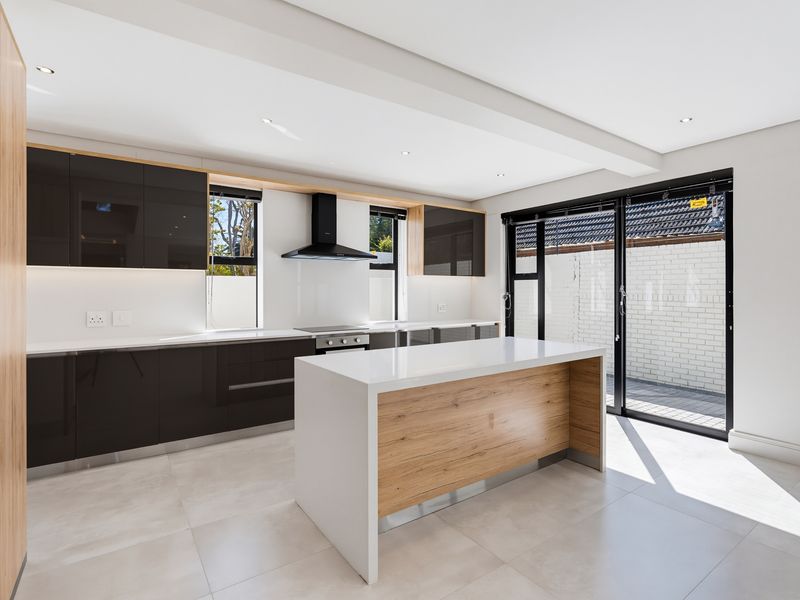 Modern kitchen featuring a central island, quartz countertops, high-gloss cabinetry, built-in appliances, and large glass sliding doors leading to an outdoor area.