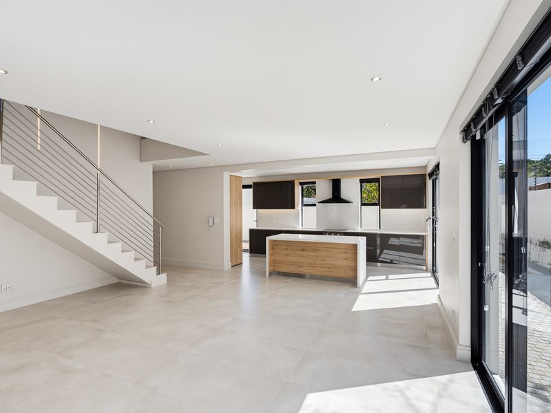 Spacious open-plan living and kitchen area featuring modern cabinetry, a central island, sleek staircase, and large sliding doors opening to the exterior.