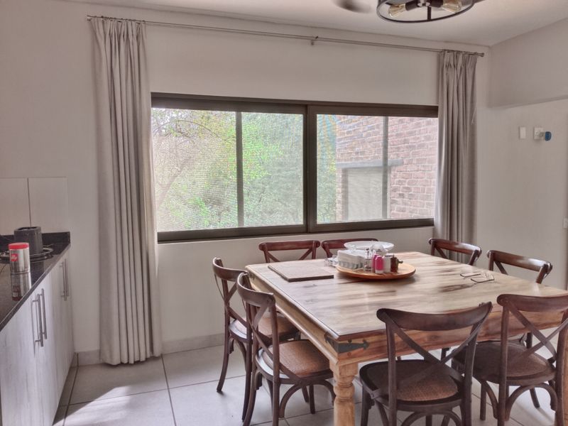 An open-plan dining area featuring large sliding windows, neutral tiled flooring, and integrated kitchen cabinetry, providing a bright and functional living space.