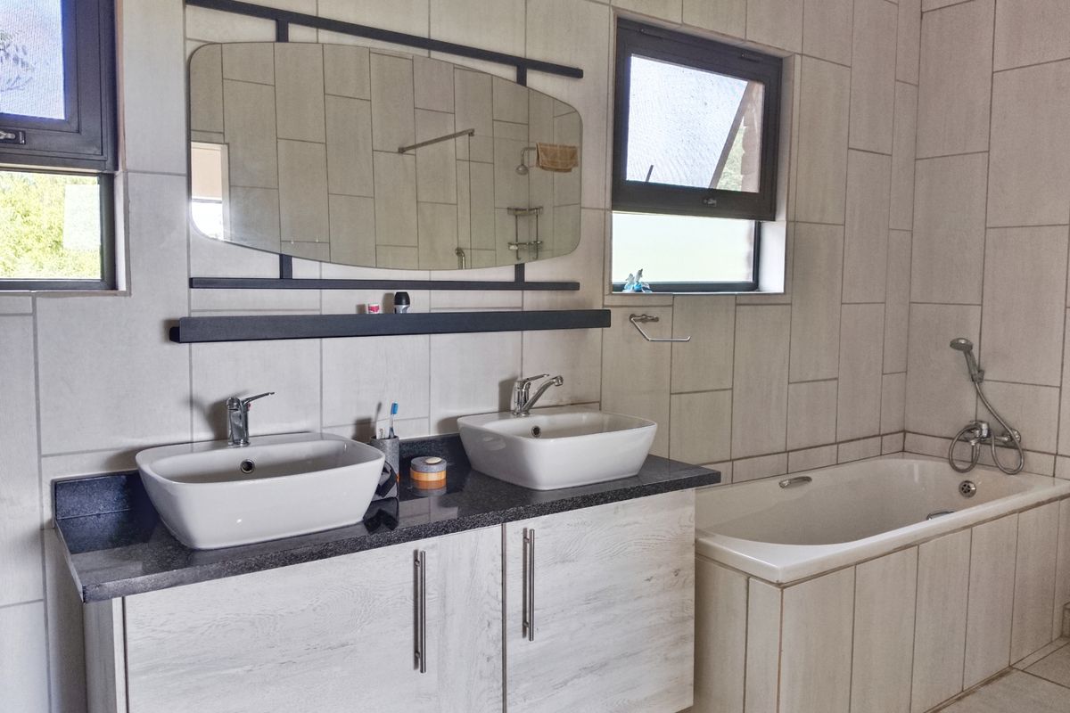 Modern bathroom featuring a double vanity with vessel sinks, a built-in bathtub with handheld shower mixer, and neutral wall tiling.