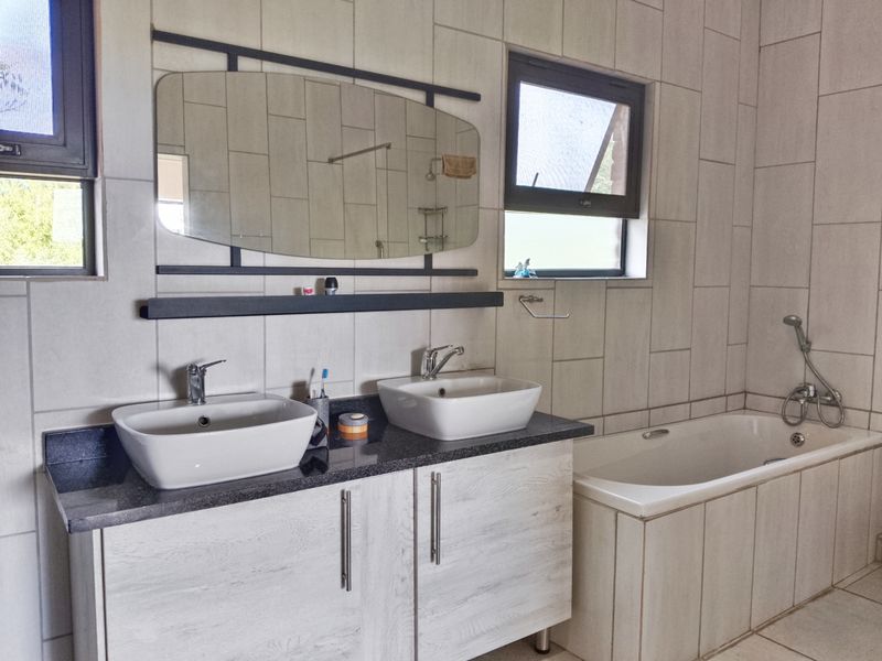 Modern bathroom featuring a double vanity with vessel sinks, a built-in bathtub with handheld shower mixer, and neutral wall tiling.