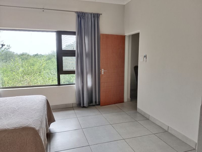 A bedroom featuring tiled flooring, a large window with natural light, and a timber door leading to an adjacent space.