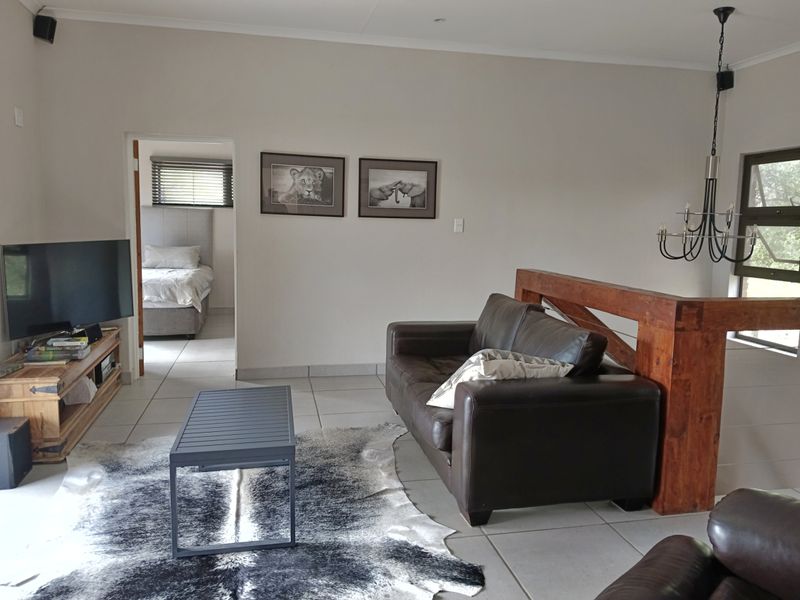 A living room featuring tiled flooring, a timber balustrade, and a pendant light fixture, with an adjacent bedroom visible through the doorway.