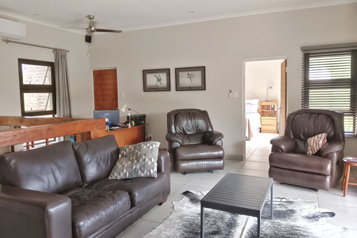 A spacious living area featuring tiled flooring, a ceiling fan, air conditioning, and a timber balustrade overlooking the lower level.