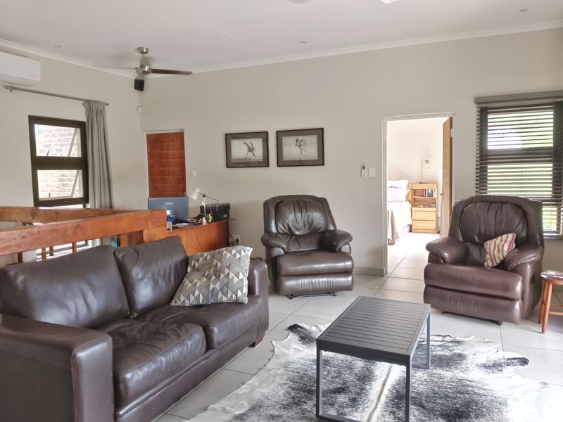 A spacious living area featuring tiled flooring, a ceiling fan, air conditioning, and a timber balustrade overlooking the lower level.
