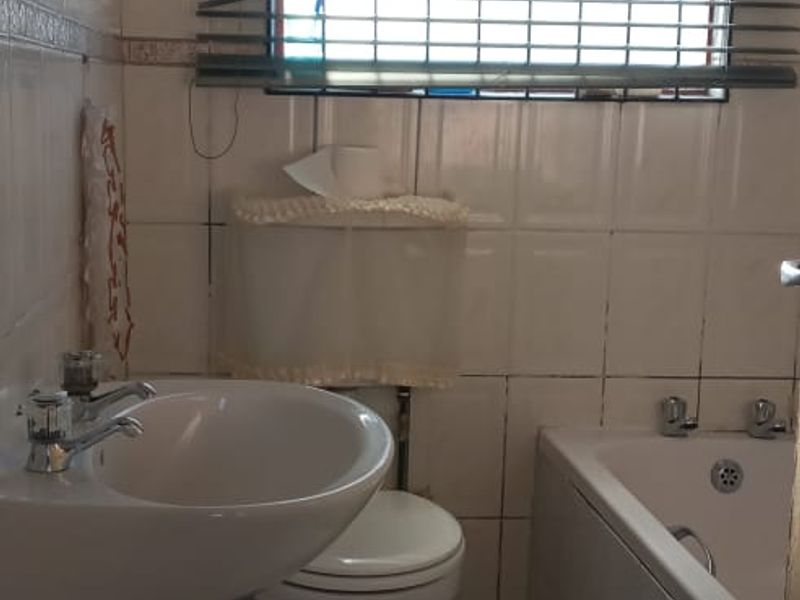 A compact bathroom featuring a pedestal basin, toilet, and bathtub with tiled finishes, requiring some maintenance and cosmetic updates.
