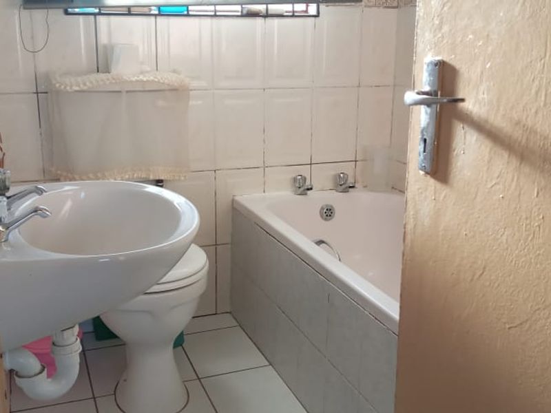 A compact bathroom featuring a pedestal washbasin, toilet, and bathtub with tiled walls and flooring, presenting a dated but functional layout.