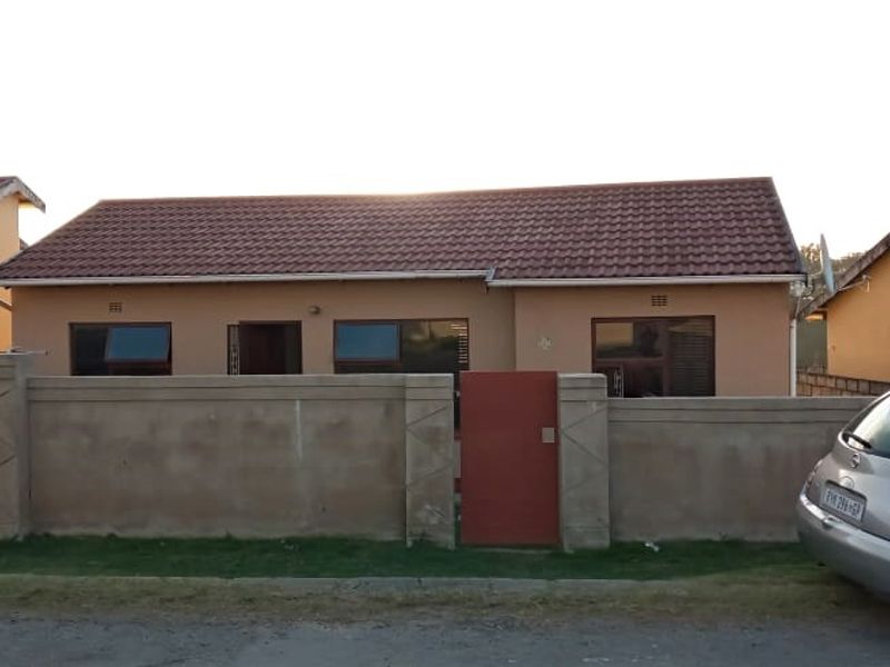 Front view of a single-story residential house featuring a tiled roof, perimeter boundary wall with a pedestrian gate, and aluminium window frames.